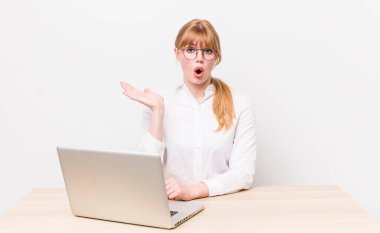 Kızıl saçlı, güzel bir kadın şaşırmış ve şok olmuş görünüyor. Çenesi düşmüş, elinde bir nesne var. iş kavramı