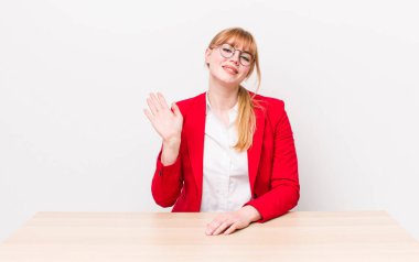 Kızıl saçlı güzel kadın mutlu bir şekilde gülümsüyor, el sallıyor, seni selamlıyor ve selamlıyor. Bağımsız kavram