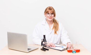 Kızıl saçlı güzel kadın mutlu bir şekilde gülümsüyor, eli kalçasında ve kendinden emin. Mikroskobik bilim adamı.