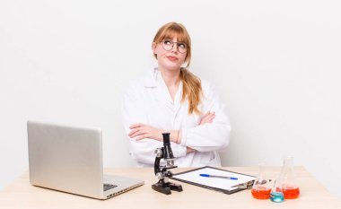 Kızıl saçlı güzel kadın omuz silkiyor, kafası karışık ve kararsız. Mikroskobik bilim adamı.