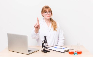 Kızıl saçlı güzel kadın gülümsüyor ve arkadaş canlısı görünüyor, bir numarayı gösteriyor. Mikroskobik bilim adamı.