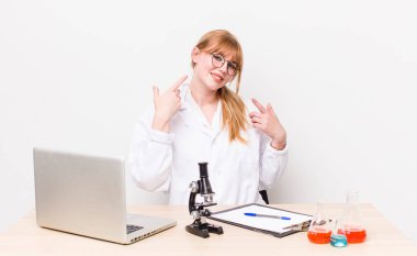 Kızıl saçlı, güzel bir kadın kendi gülüşünü işaret ediyor. Mikroskobik bilim adamı.