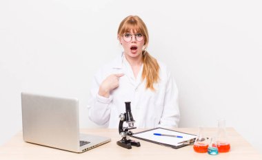 Kızıl saçlı güzel kadın şok olmuş ve ağzı açık, kendini işaret eden bir şekilde şaşırmış görünüyor. Mikroskobik bilim adamı.