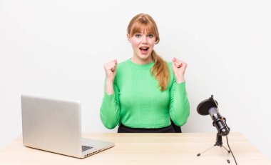 Kızıl saçlı güzel kadın şok olmuş hissediyor, gülüyor ve başarıyı kutluyor. dizüstü bilgisayar ve mikrofon kavramı