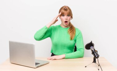 Kızıl saçlı güzel kadın mutlu, şaşkın ve şaşırmış görünüyor. dizüstü bilgisayar ve mikrofon kavramı
