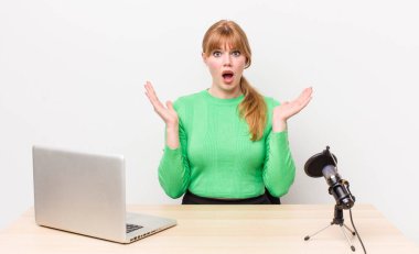 Kızıl saçlı güzel kadın kendini mutlu hissediyor ve inanılmaz bir şeye hayret ediyor. dizüstü bilgisayar ve mikrofon kavramı