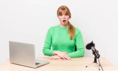 Kızıl saçlı güzel kadın çok şaşırmış ya da şaşkın görünüyor. dizüstü bilgisayar ve mikrofon kavramı