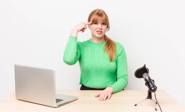 Kızıl saçlı güzel kadın kafası karışık ve şaşkın hissediyor, deli olduğunu gösteriyor. dizüstü bilgisayar ve mikrofon kavramı