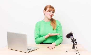 kızıl saçlı güzel bir kadın neşeli bir şekilde gülümsüyor, mutlu hissediyor ve bir konsept gösteriyor. dizüstü bilgisayar ve mikrofon kavramı