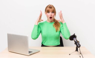 Kızıl saçlı güzel kadın ellerini havaya kaldırarak çığlık atıyor. dizüstü bilgisayar ve mikrofon kavramı