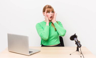 Kızıl saçlı güzel kadın mutlu, heyecanlı ve şaşırmış hissediyor. dizüstü bilgisayar ve mikrofon kavramı