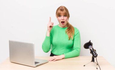 Kızıl saçlı, güzel bir kadın bir fikri fark ettikten sonra mutlu ve heyecanlı bir dahi gibi hissediyor. dizüstü bilgisayar ve mikrofon kavramı