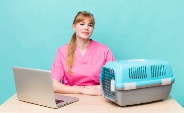 Kızıl saçlı güzel kadın mutlu bir şekilde gülümsüyor, eli kalçasında ve kendinden emin. Veterinerlik kavramı