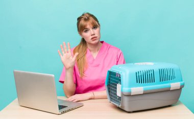 Kızıl saçlı güzel kadın ciddi görünüyor. Avuç içini gösteriyor. Durdurma hareketi yapıyor. Veterinerlik kavramı