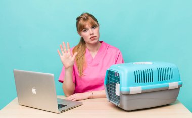 Kızıl saçlı güzel kadın ciddi görünüyor. Avuç içini gösteriyor. Durdurma hareketi yapıyor. Veterinerlik kavramı