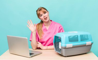 Kızıl saçlı güzel kadın mutlu bir şekilde gülümsüyor, el sallıyor, seni selamlıyor ve selamlıyor. Veterinerlik kavramı