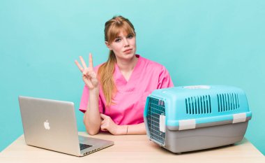 Kızıl saçlı güzel kadın gülümsüyor ve arkadaş canlısı görünüyor, üç numarayı gösteriyor. Veterinerlik kavramı