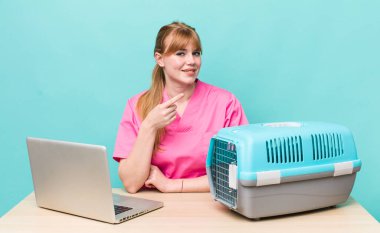 Kızıl saçlı güzel bir kadın neşeyle gülümsüyor, mutlu hissediyor ve bir tarafı işaret ediyor. Veterinerlik kavramı