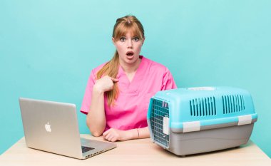 Kızıl saçlı güzel kadın şok olmuş ve ağzı açık, kendini işaret eden bir şekilde şaşırmış görünüyor. Veterinerlik kavramı