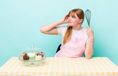 Kızıl saçlı güzel kadın şaşkın ve kafası karışık, kaşınan bir kafa hissediyor. Ev yapımı kek konsepti