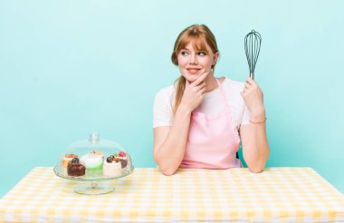 Kızıl saçlı, güzel bir kadın mutlu, kendinden emin, elleri çenesinde gülümsüyor. Ev yapımı kek konsepti