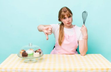 Kızıl saçlı, güzel bir kadın kendini kötü hissediyor, baş parmağını kaldırıyor. Ev yapımı kek konsepti