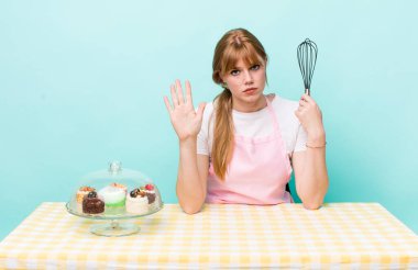 Kızıl saçlı güzel kadın ciddi görünüyor. Avuç içini gösteriyor. Durdurma hareketi yapıyor. Ev yapımı kek konsepti