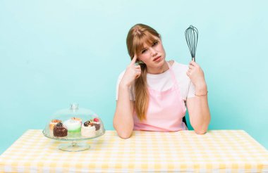 Kızıl saçlı güzel kadın kafası karışık ve şaşkın hissediyor, deli olduğunu gösteriyor. Ev yapımı kek konsepti