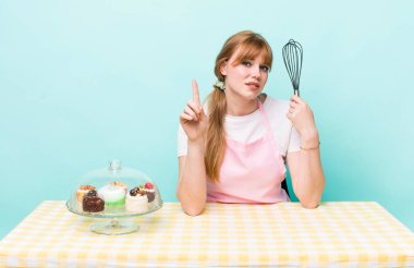 Kızıl saçlı güzel kadın gülümsüyor ve arkadaş canlısı görünüyor, bir numarayı gösteriyor. Ev yapımı kek konsepti