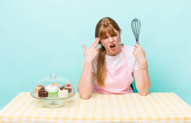 Kızıl saçlı güzel bir kadın mutsuz ve stresli görünüyor, intihar jesti silah işareti yapıyor. Ev yapımı kek konsepti