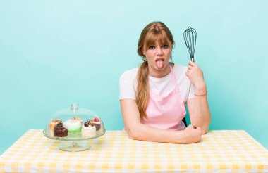 Kızıl saçlı güzel kadın iğrenmiş ve sinirlenmiş hissediyor ve dilini dışarı çıkarıyor. Ev yapımı kek konsepti