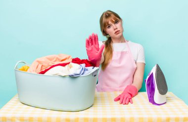 Kızıl saçlı güzel kadın ciddi görünüyor. Avuç içini gösteriyor. Durdurma hareketi yapıyor. Demir giysi konsepti