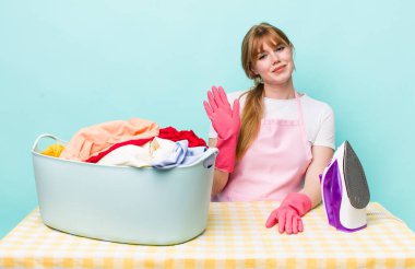 Kızıl saçlı güzel kadın mutlu bir şekilde gülümsüyor, el sallıyor, seni selamlıyor ve selamlıyor. Demir giysi konsepti