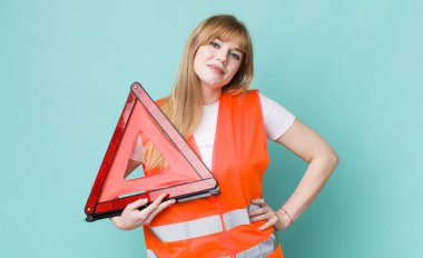 Kızıl saçlı güzel kadın mutlu bir şekilde gülümsüyor, eli kalçasında ve kendinden emin. araba acil üçgeni