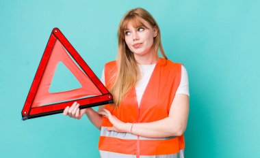 Kızıl saçlı güzel kadın omuz silkiyor, kafası karışık ve kararsız. araba acil üçgeni