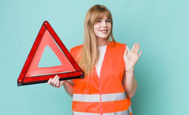 Kızıl saçlı güzel kadın mutlu bir şekilde gülümsüyor, el sallıyor, seni selamlıyor ve selamlıyor. araba acil üçgeni