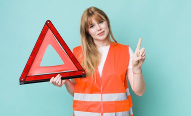 Kızıl saçlı güzel kadın gülümsüyor ve arkadaş canlısı görünüyor, bir numarayı gösteriyor. araba acil üçgeni