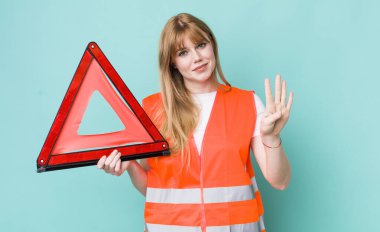 Kızıl saçlı güzel kadın gülümsüyor ve arkadaş canlısı görünüyor, dört numarayı gösteriyor. araba acil üçgeni