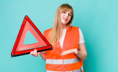 kızıl saçlı güzel bir kadın neşeli bir şekilde gülümsüyor, mutlu hissediyor ve bir konsept gösteriyor. araba acil üçgeni