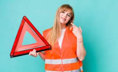 Kızıl saçlı, güzel bir kadın kendi gülüşünü işaret ediyor. araba acil üçgeni