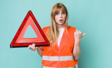 Kızıl saçlı, güzel bir kadın inançsızlıktan şaşkın şaşkın bakıyor. araba acil üçgeni