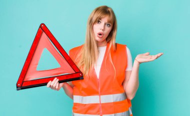 Kızıl saçlı, güzel bir kadın şaşırmış ve şok olmuş görünüyor. Çenesi düşmüş, elinde bir nesne var. araba acil üçgeni