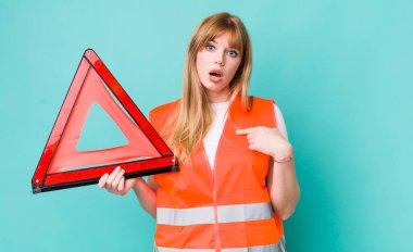 Kızıl saçlı güzel kadın şok olmuş ve ağzı açık, kendini işaret eden bir şekilde şaşırmış görünüyor. araba acil üçgeni