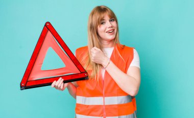 Kızıl saçlı güzel bir kadın kendini mutlu hissediyor ve bir meydan okumayla yüzleşiyor ya da kutluyor. araba acil üçgeni