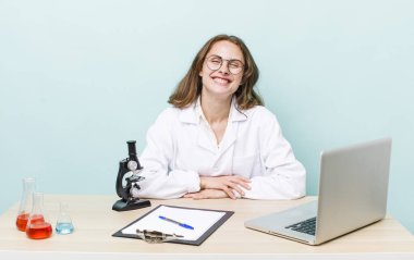 Genç ve güzel bir kadın mutlu bir şekilde gülümsüyor, eli kalçasında ve kendinden emin. Mikroskop konseptine sahip bilim adamı