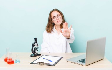 Genç ve güzel bir kadın ciddi görünüyor. Avuç içini gösteriyor. Durdurma hareketi yapıyor. Mikroskop konseptine sahip bilim adamı