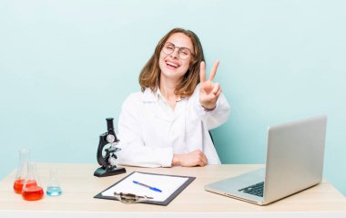 Genç, güzel bir bayan gülümsüyor ve iki numarayı gösteriyor. Mikroskop konseptine sahip bilim adamı