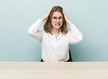 Genç ve güzel bir kadın gergin, endişeli ya da korkmuş hissediyor. Elleri başının üstünde. masa ve iş konsepti