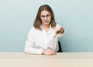Genç ve güzel bir kadın kendini kötü hissediyor, baş parmağını kaldırıyor. masa ve iş konsepti