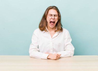 Genç ve güzel bir kadın agresif bir şekilde bağırıyor, çok kızgın görünüyor. masa ve iş konsepti
